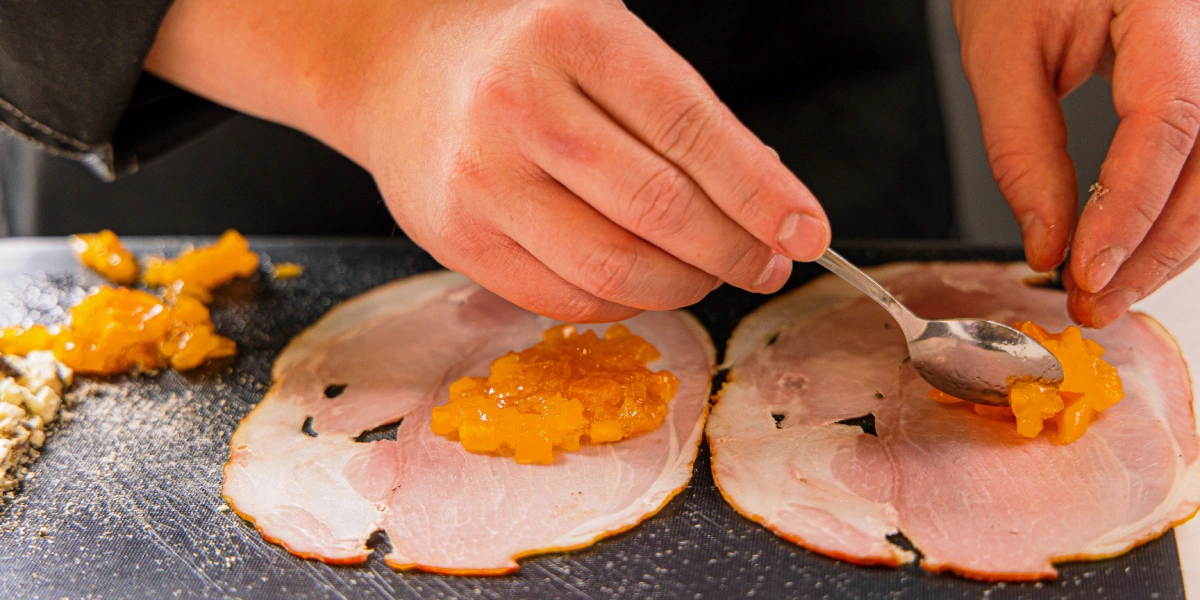 Выложите на&nbsp;ломтики окорока измельчённую хурму и&nbsp;сыр